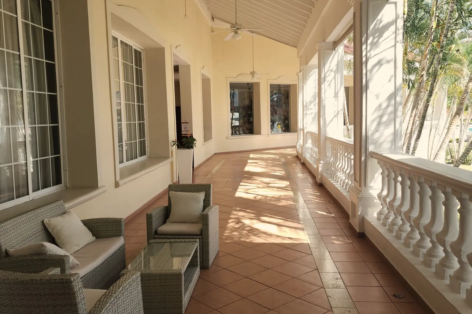 A long covered stoep with red tiles, a white balustrade, wicker chairs and ceiling fans