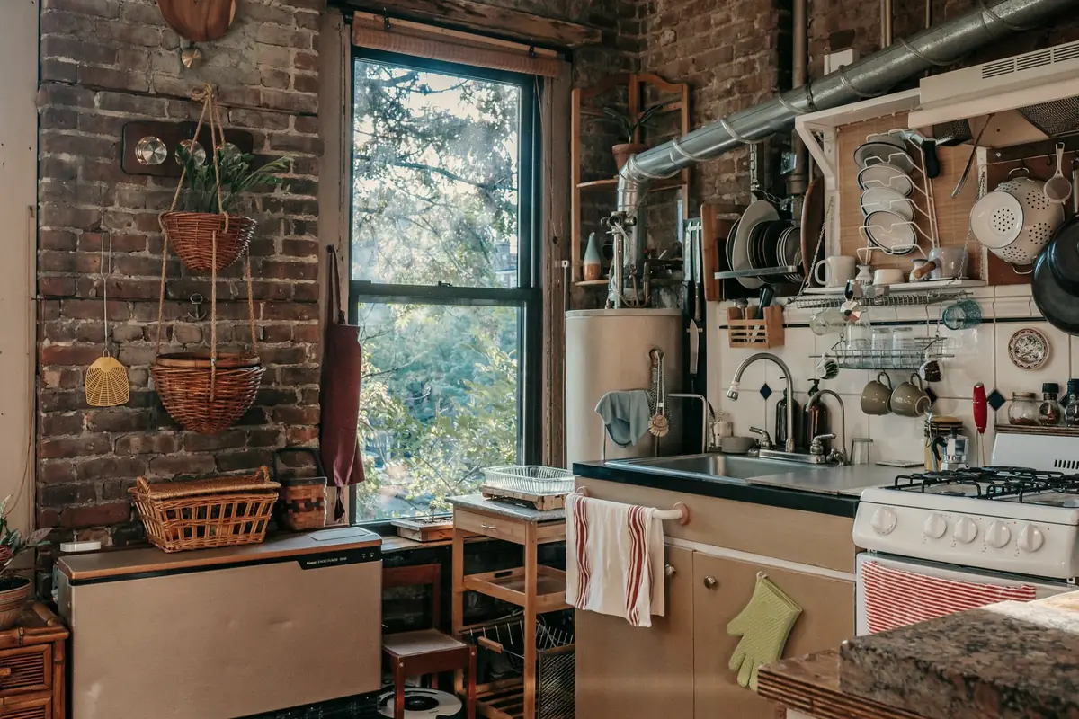 A kitchen with an exposed brick wall, a gas stove and hanging pots