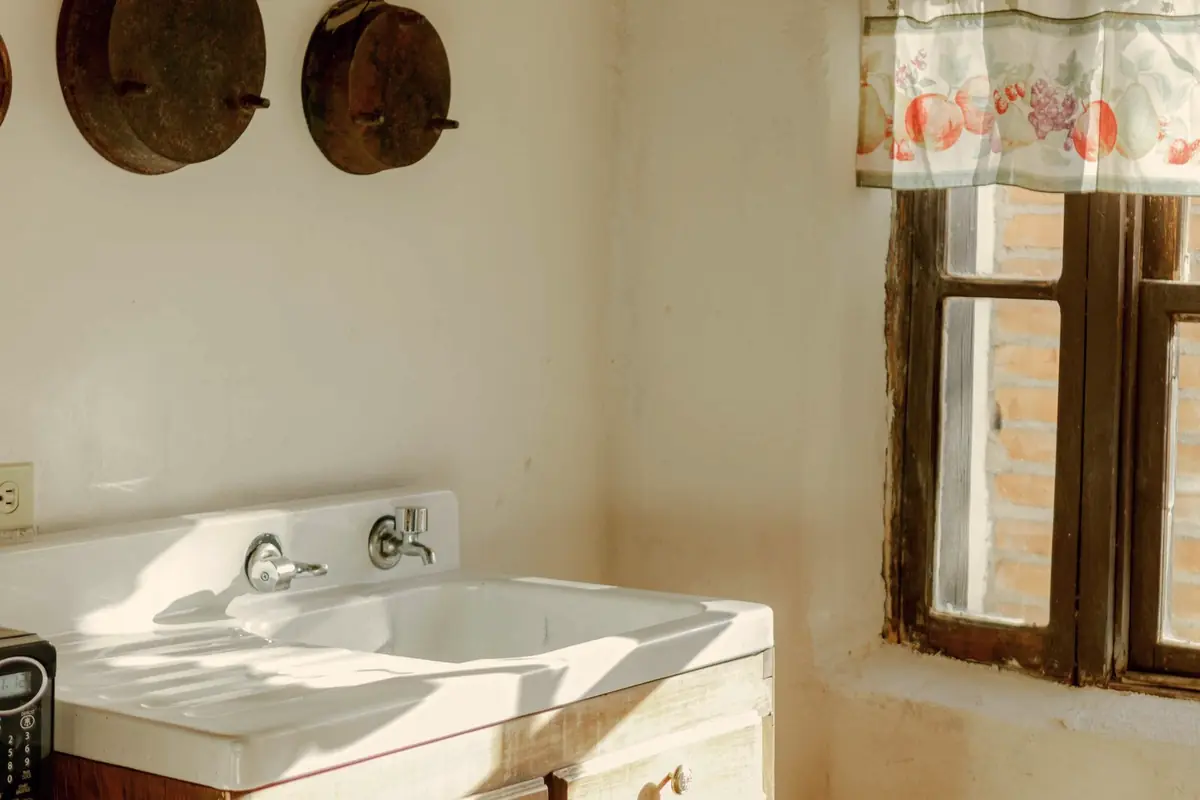 A small bright kitchen with a cream sink cabinet and a window above it