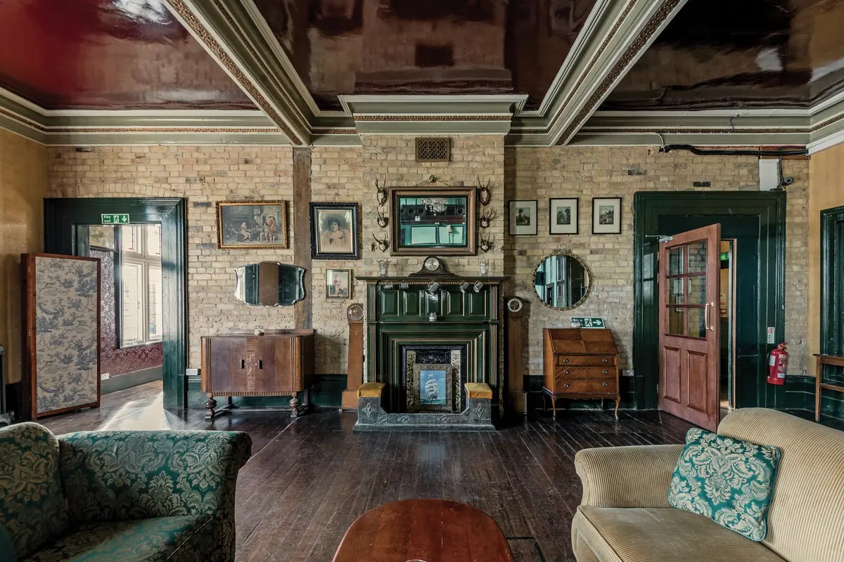 A lounge with an old fireplace, timber floors and a mix of vintage furniture