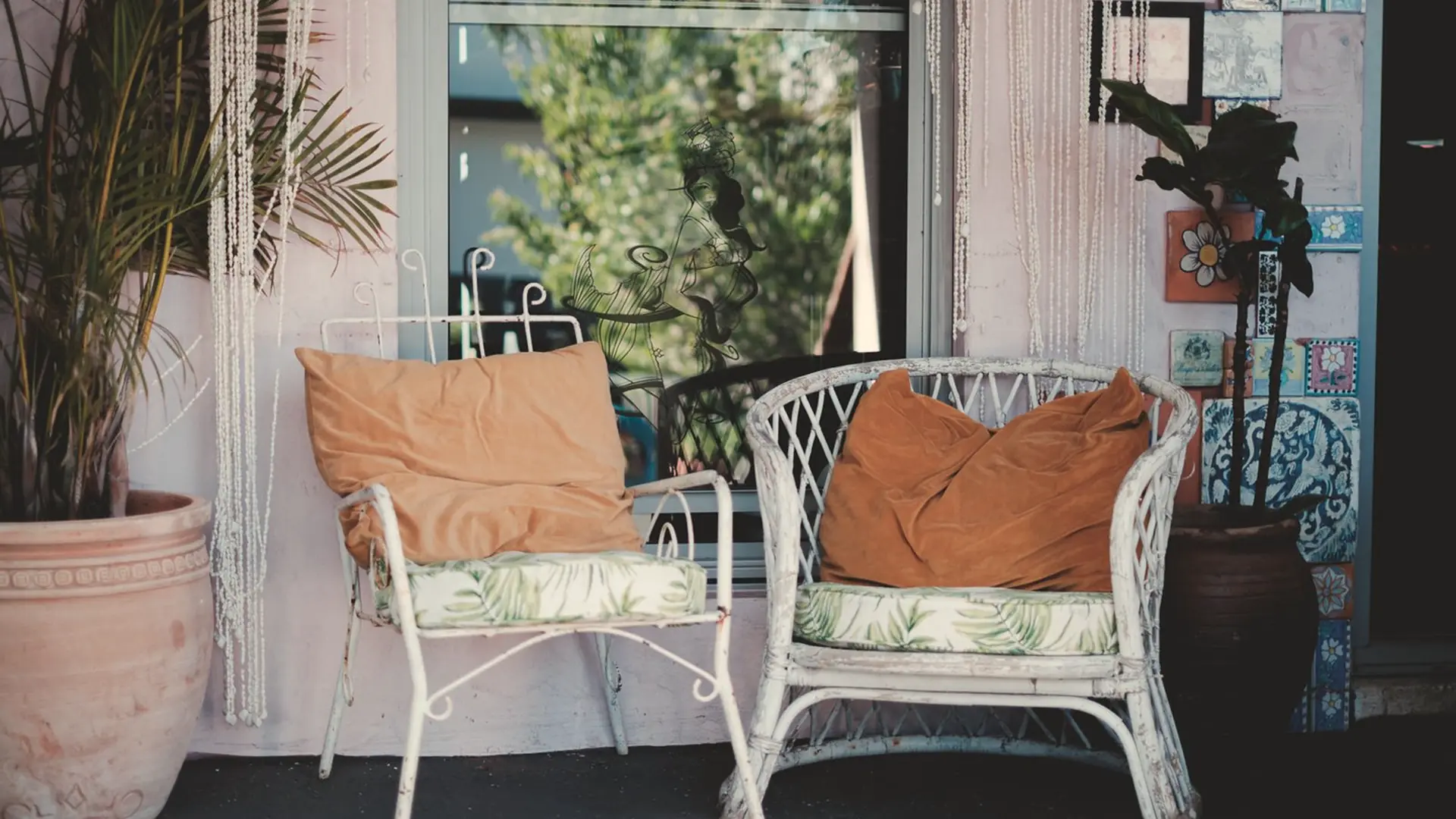 Two wicker chairs with cushions beside a window and pot plants